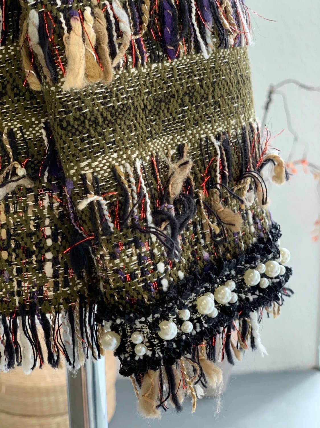 Olive-green couture tweed with red metallic threading, fringed edge, and pearl-trimmed black braid