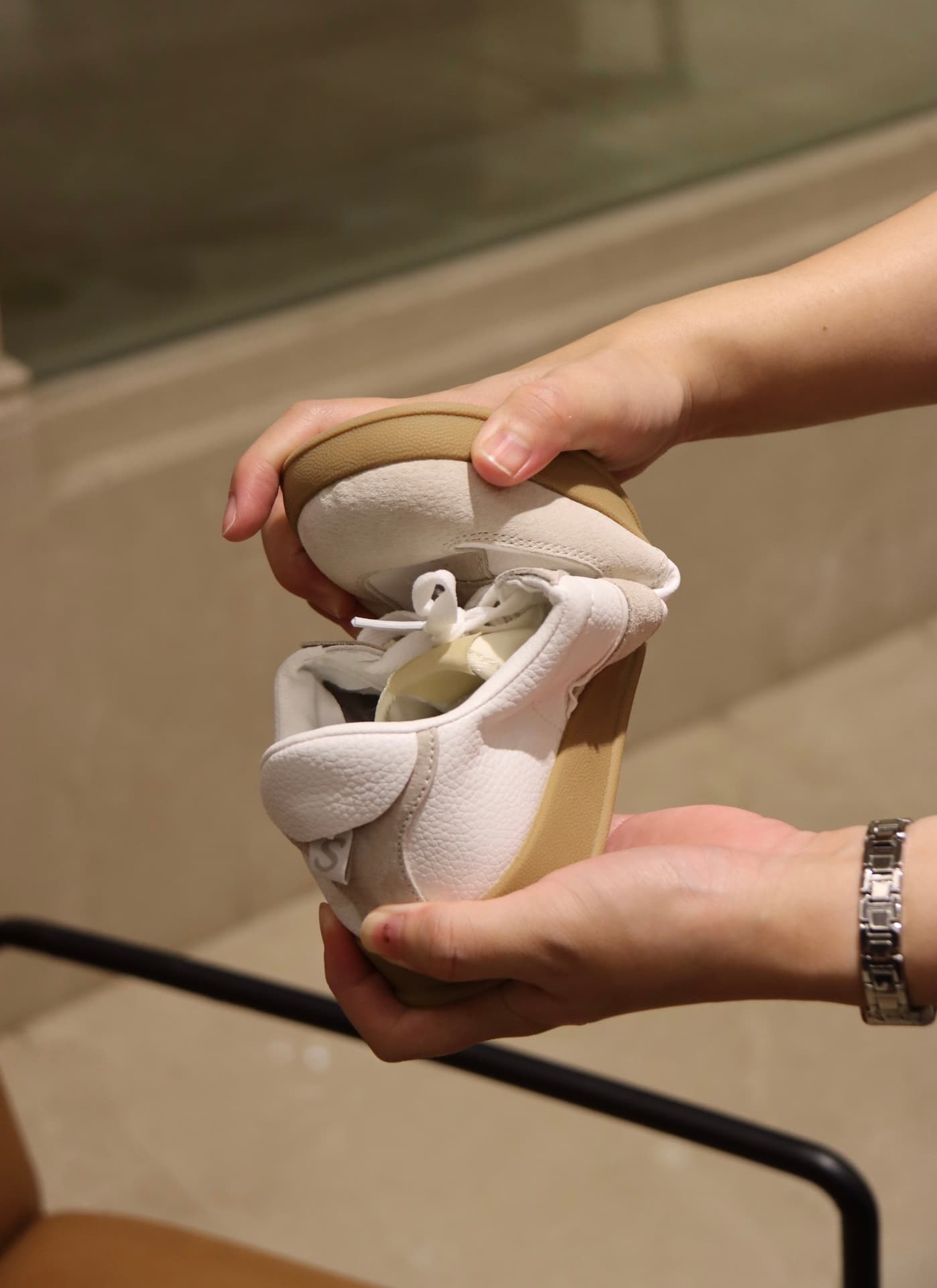 Two hands flexing the sole of a white sneaker with tan welt — a tactile flex test on the production floor