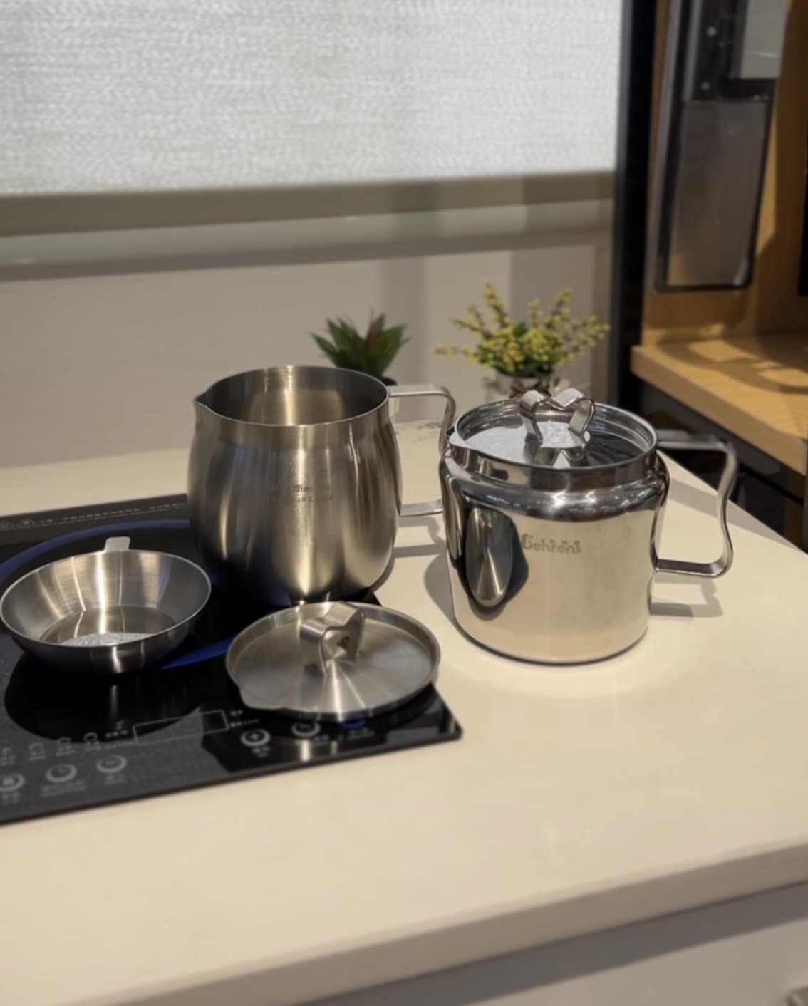 Stainless steel cookware set, pot with lid, milk pan, and bowl, on a kitchen counter